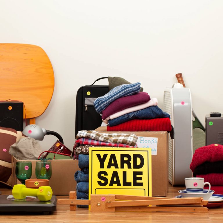 Bunch of used objects in garage with yellow "Yard Sale" sign in front.
