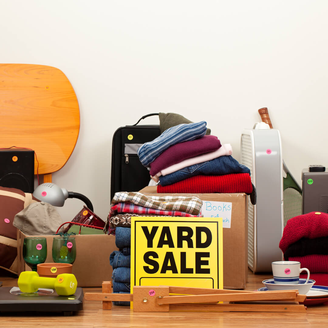 Bunch of used objects in garage with yellow "Yard Sale" sign in front.