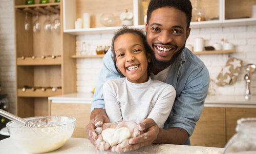 Father and daughter in kitchen baking, looking at the camera and smiling.