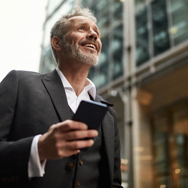 Businessman in 50s walking down street with mobile phone, ready for interview.