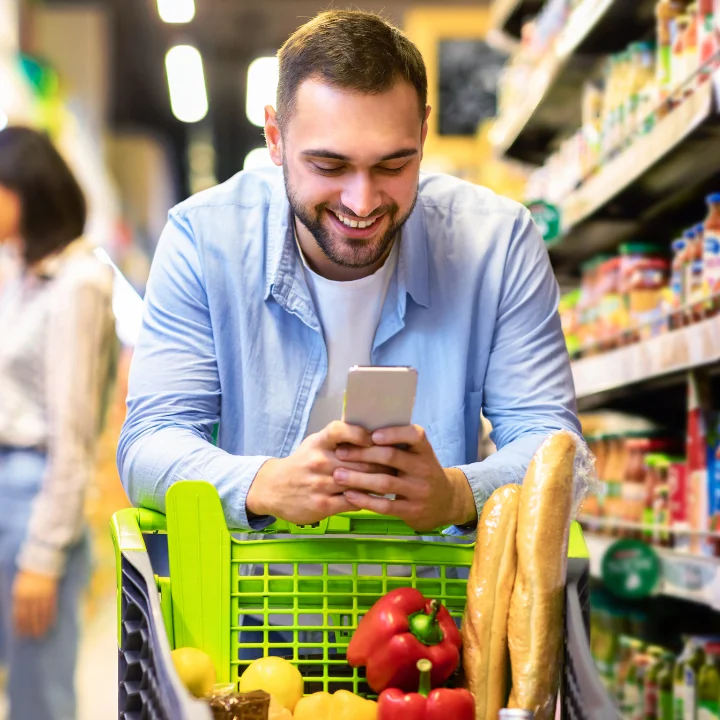 A man happily shops in a grocery store, checking his balance on the Quorum online banking app on his cell phone. “A man happily shops in a grocery store, checking his balance on the Quorum online banking app on his cell phone.