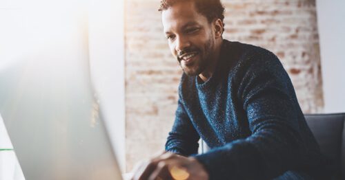 Man smiles and looks at this laptop.