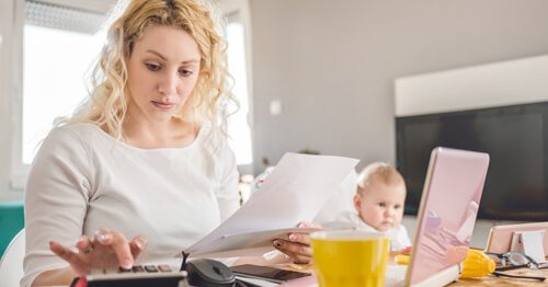Concerned mother crunching childcare costs with young baby in background.