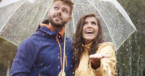 Couple smiling under umbrella, protected from rain.