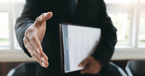 Employer holding resume and extending hand as if to welcome a new hire to a new job.