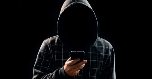 Scammer dressed all in black, holding mobile phone.