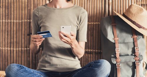 Closeup of woman sitting with a phone and credit card in her hands, planning her next vacation.