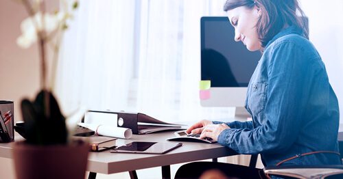 Woman at desk, smiling, working on taxes, entering numbers into a calculator.