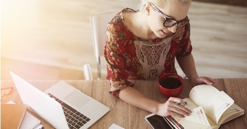 Closeup of woman using calendar, along with her phone and laptop.