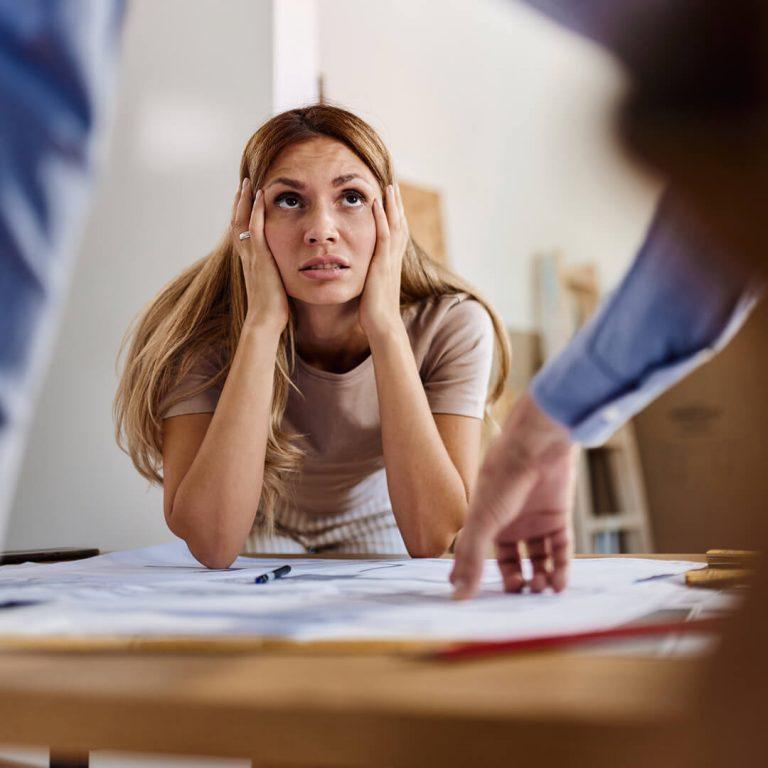 Worried woman talking about blueprint problems with a contractor (and possible scammer) in her house.