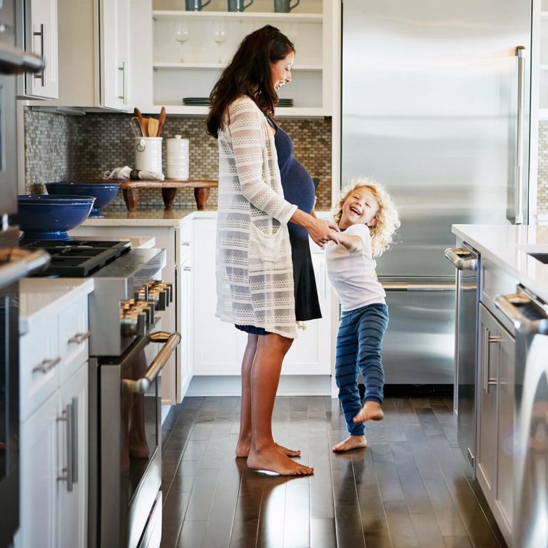 Mother and child in kitchen, surrounded by home appliances.