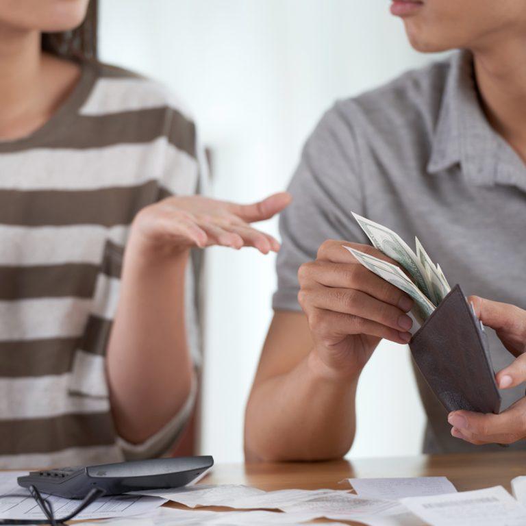 Couple discussing sharing expenses at table, with wallet, calculator and bills.