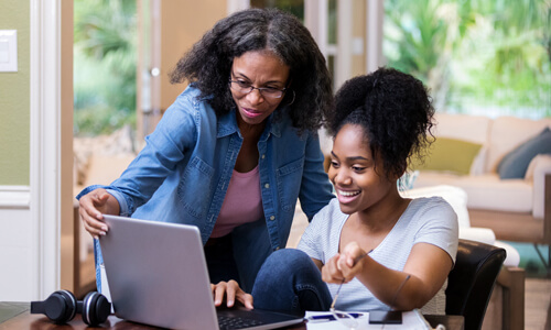 Mother helping her adult daughter review her finances at kitchen table.