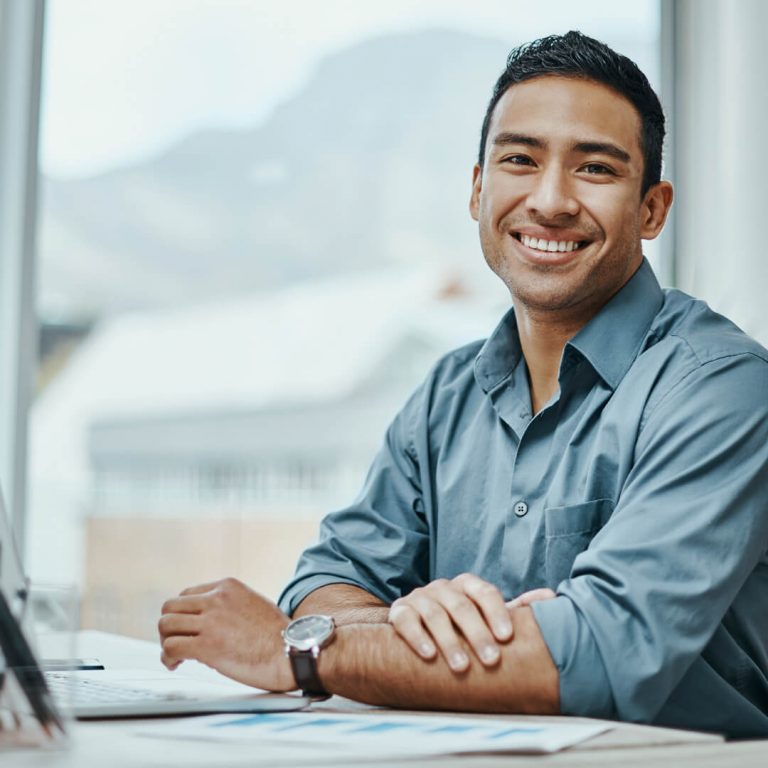 Young, well-dressed man at office desk, smiling at office.