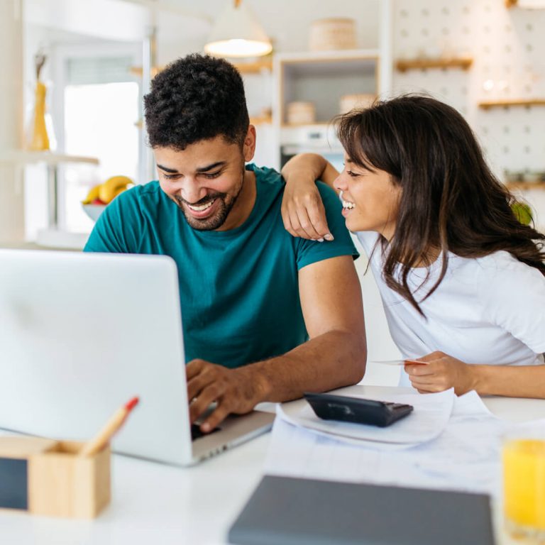 Young couple sit at counter with laptop talking about finances.