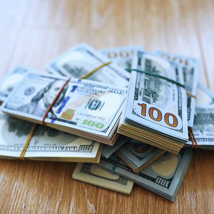 Stack of hundred dollar bills on table, signifying abandoned property and unclaimed funds.