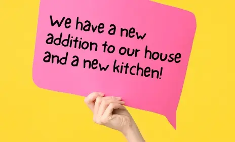 A hand holding a sign that says "We have a new addition to our house and a new kitchen."