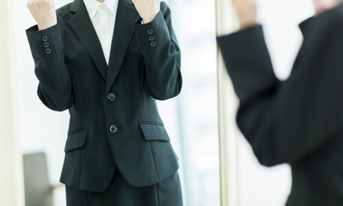 Happy woman stands in front of mirror in business clothes, happy she saved money on her wardrobe.