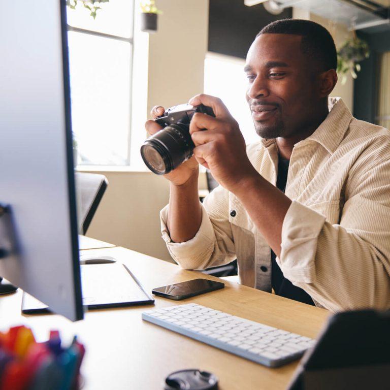 Man sits at his computer monitor, examining his new digital camera, his latest hobby.
