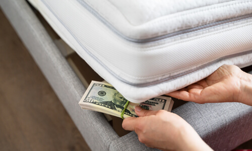Stack of fifty dollar bills being stashed under mattress.