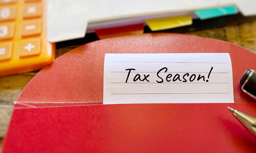 Red folder labeled "tax season!" with colored folders in background and yellow calculator on side.
