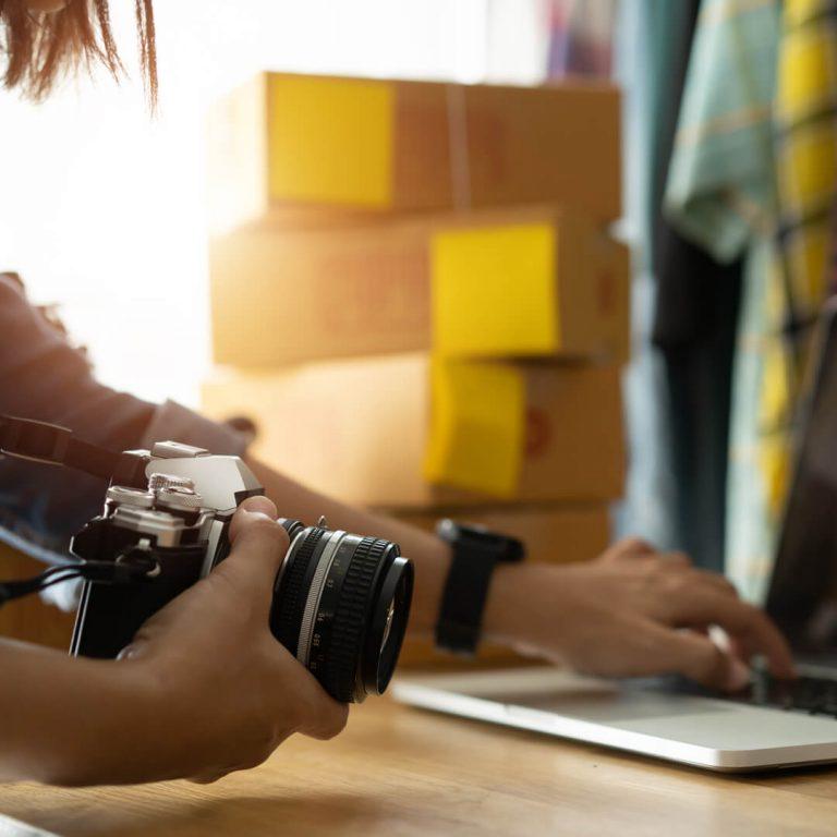 Woman with camera and laptop readying luxury item for sale online.