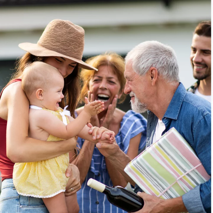 At an outdoor family gathering a grandfather clasps the hand of his baby grand daughter.