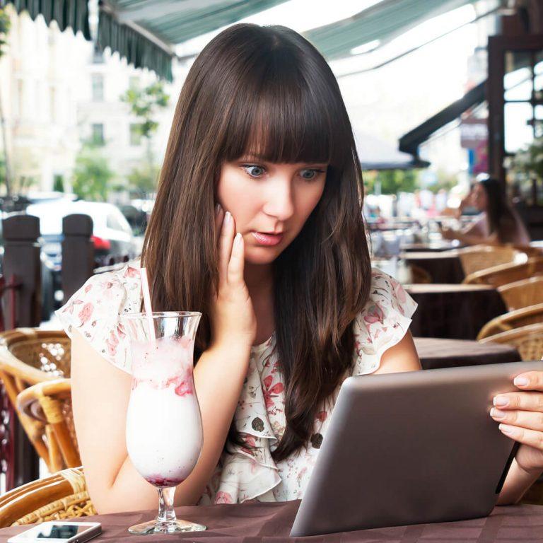Young woman on vacation looks at tablet in concern, worried she may be victim of scam.