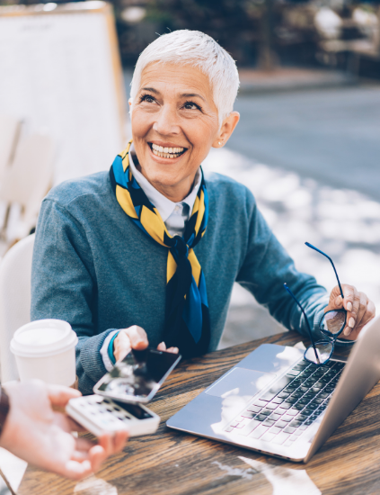 Woman in her 50s using her iPhone to make a payment at an outdoor cafe.